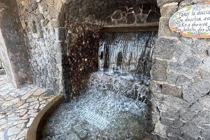 A stone water feature with a sign in a foreign language, a stone wall, and a tiled floor. 3
