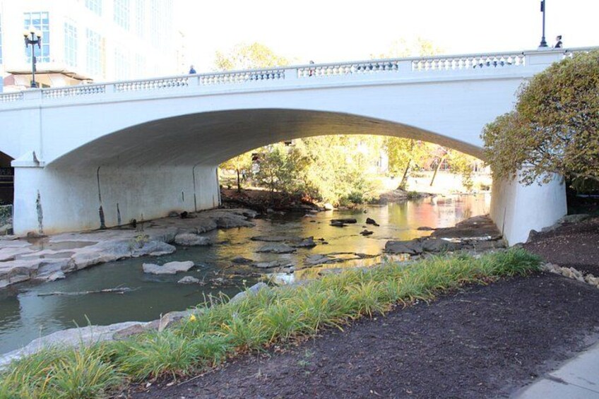 A stone bridge over a calm river with rocks and greenery around. 2