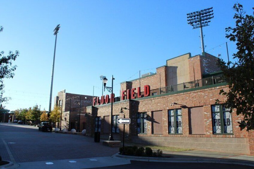 A brick building with 'ELKOR FIELD' signage, a street, and a clear sky. 5