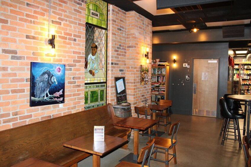 A brick-walled cafe with wooden tables and chairs, a mural, and a bar area with shelves of bottles. 3