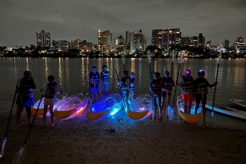 People in canoes on a beach with city buildings in the background. 4