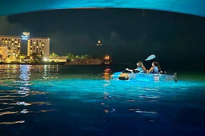 A nighttime scene with a boat on a body of water, a building with lights in the background, and a clear sky. 3