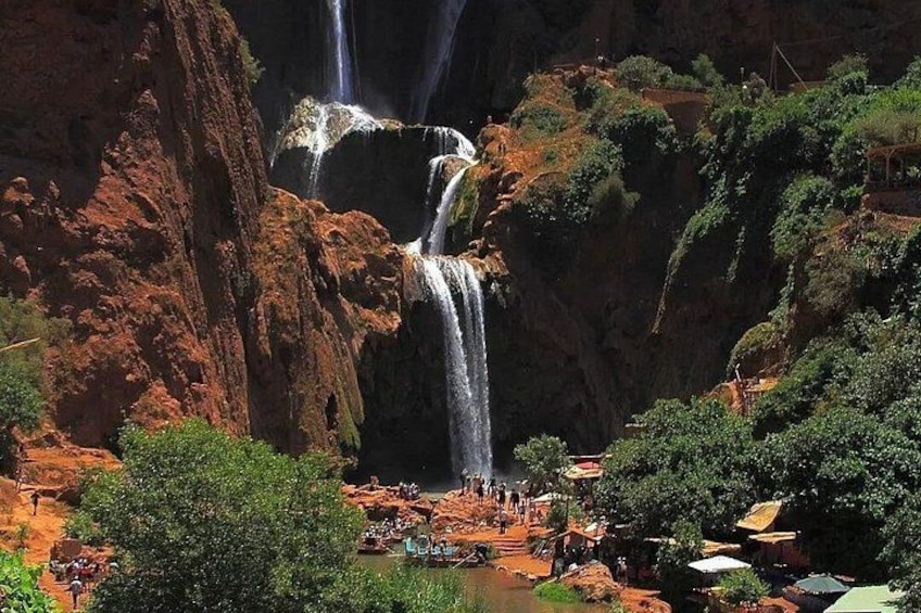 A waterfall cascading down a rocky cliff surrounded by lush greenery and a small settlement with people and boats. 4