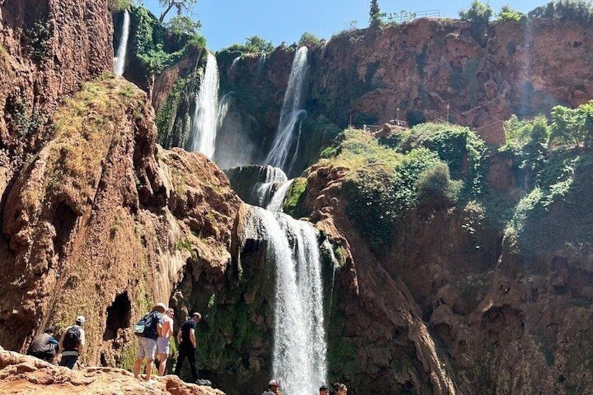 A waterfall cascading down a rocky cliff with hikers in the foreground. 1