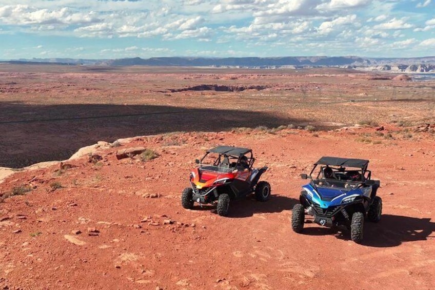 Two off-road vehicles parked on a red desert landscape with distant mountains. 1
