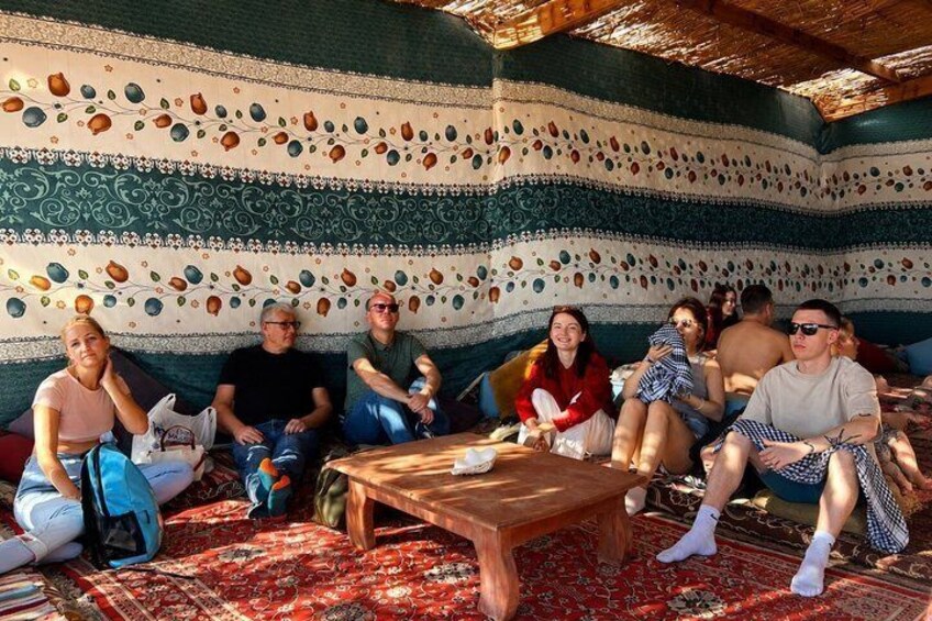 A group of people sitting on a patterned carpet in a room with a wooden table. 5