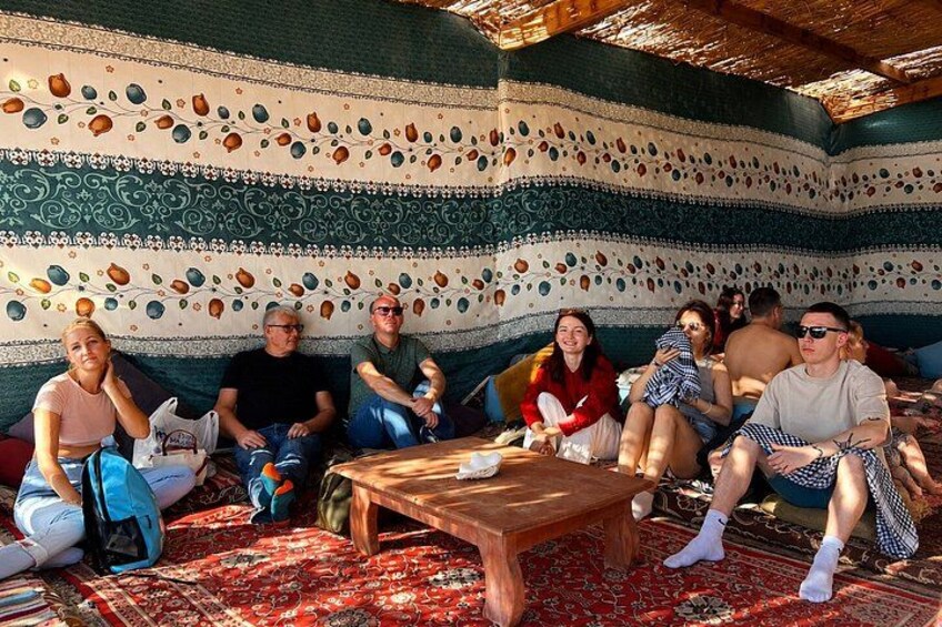 A group of people sitting on a patterned rug in a room with a wooden table. 5
