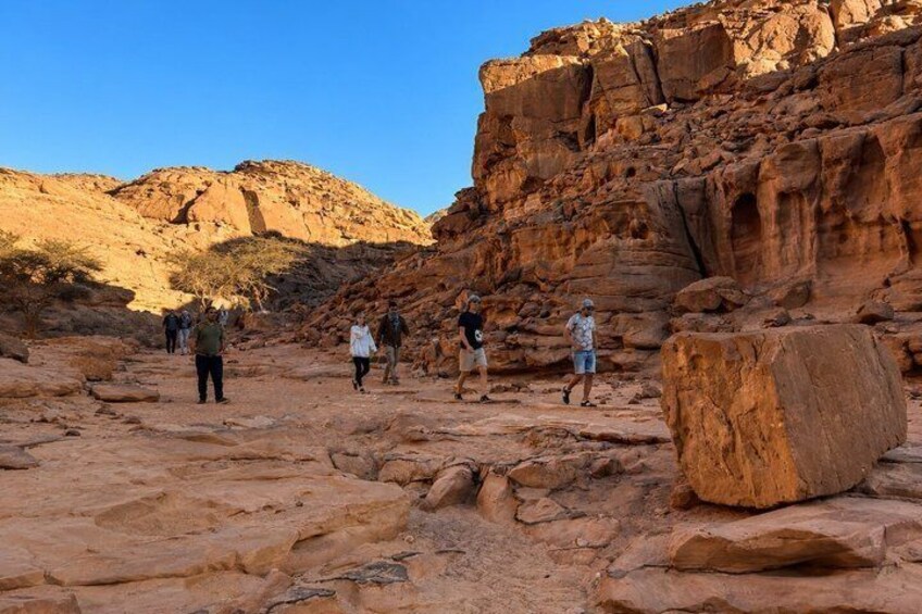 A group of people hiking in a rocky desert landscape with large boulders and a clear blue sky. 3