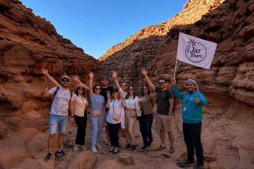 A group of people in a canyon with a flag reading 'Jaz Tours.' 1
