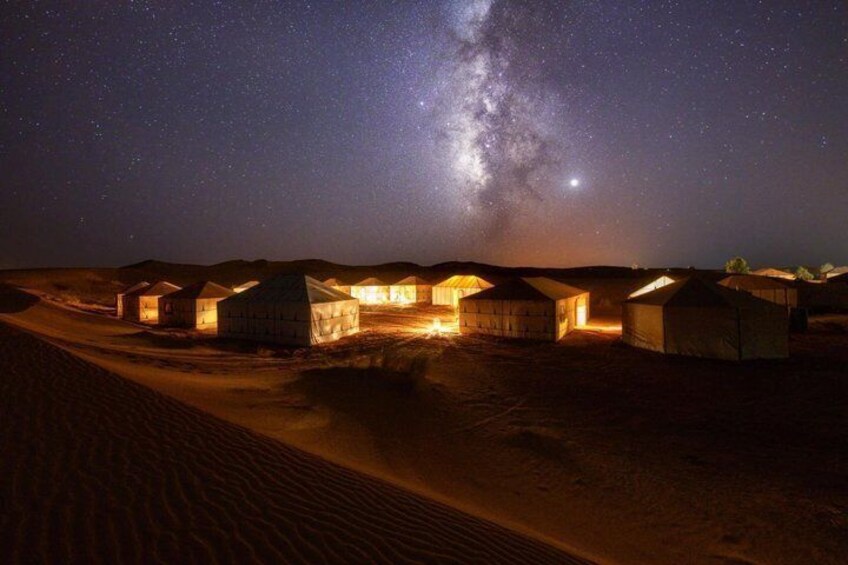 A desert landscape with illuminated tents under a starry night sky. 3