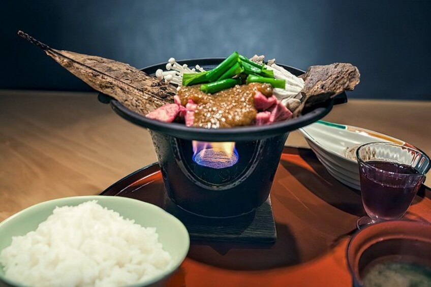 A hot pot meal with various meats and vegetables, a bowl of white rice, and a glass of purple drink on a wooden table. 2
