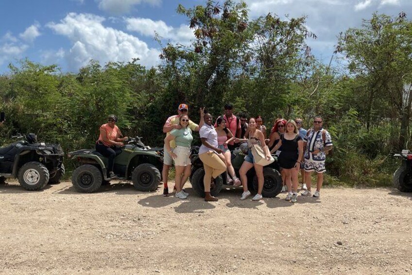 A group of people posing with ATVs on a dirt path surrounded by greenery. 2