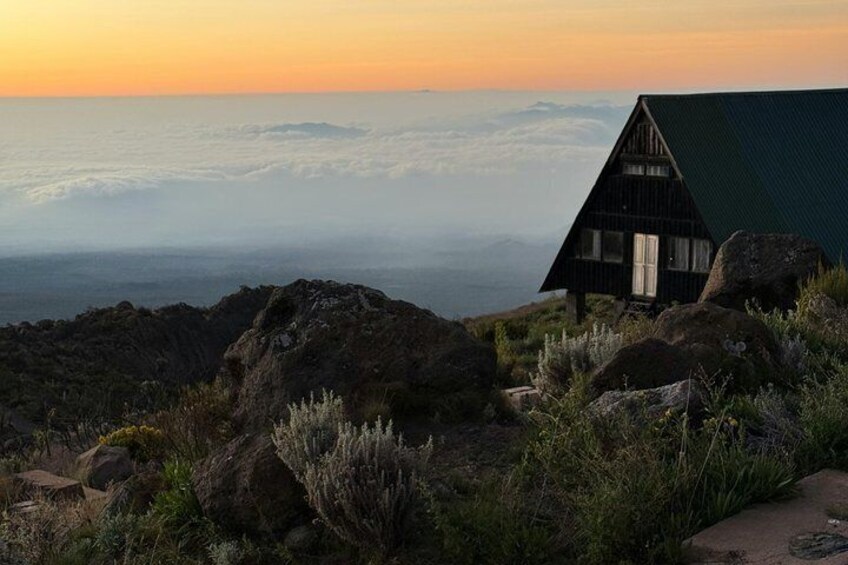 A wooden cabin with a green roof overlooking a mountainous landscape at sunset. 3