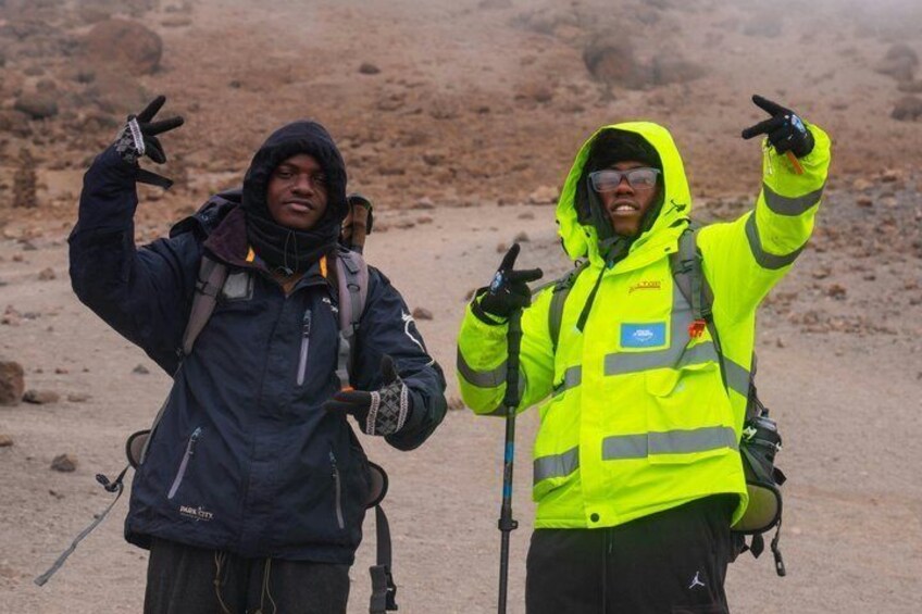 Two individuals in outdoor gear, one in dark and one in bright yellow, standing on a rocky terrain. 3