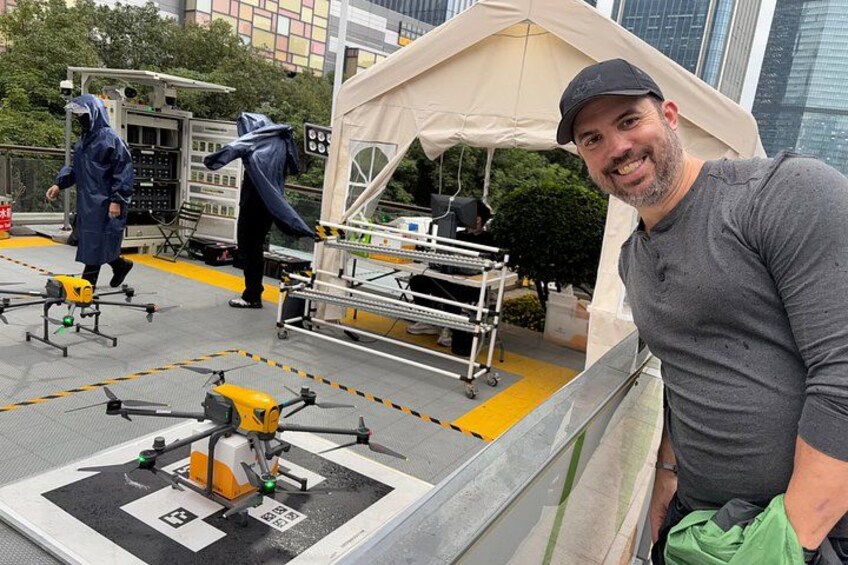 A man standing near drones on a rooftop with a tent and equipment in the background. 3