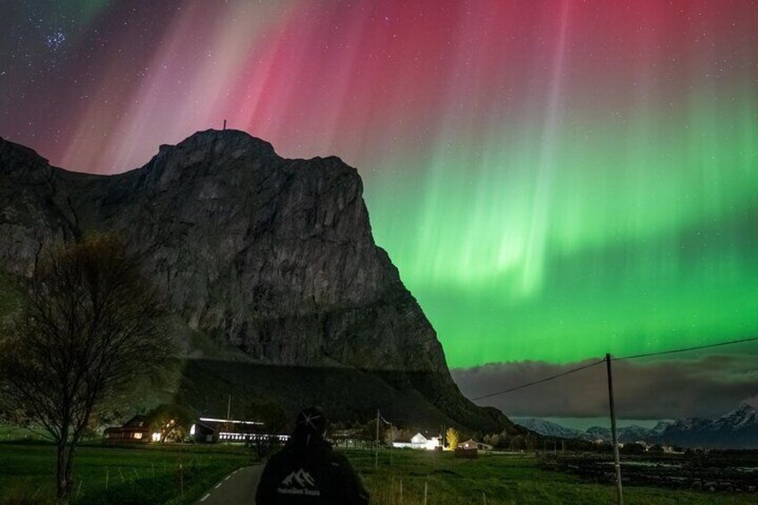 A mountain with aurora borealis, a road, and a building with lights. 5