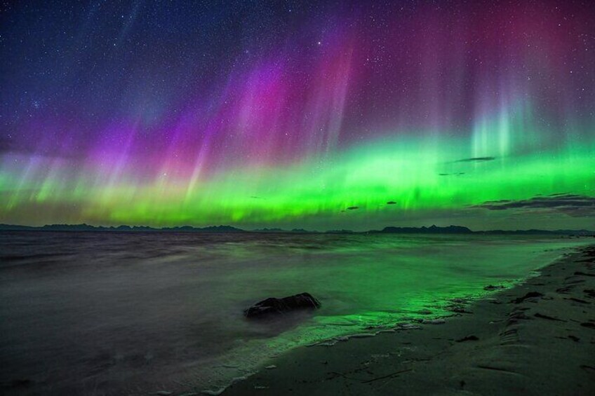 The Northern Lights over a snowy landscape with a rock in the foreground. 3