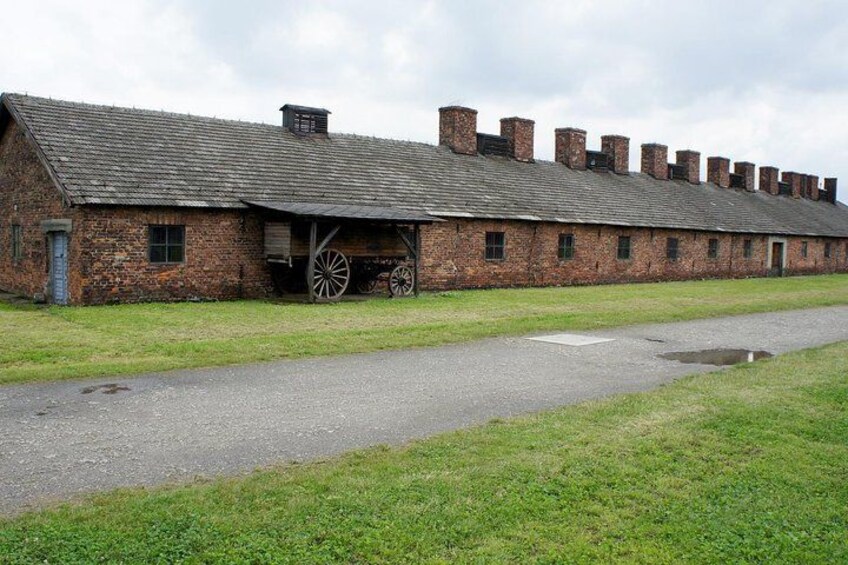 A brick building with a large wooden wheel, a grassy area, and a paved path. 2
