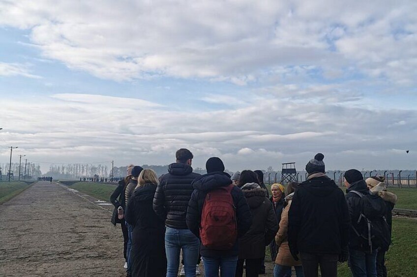 A group of people standing on a dirt path, facing a body of water with a cloudy sky above. 3