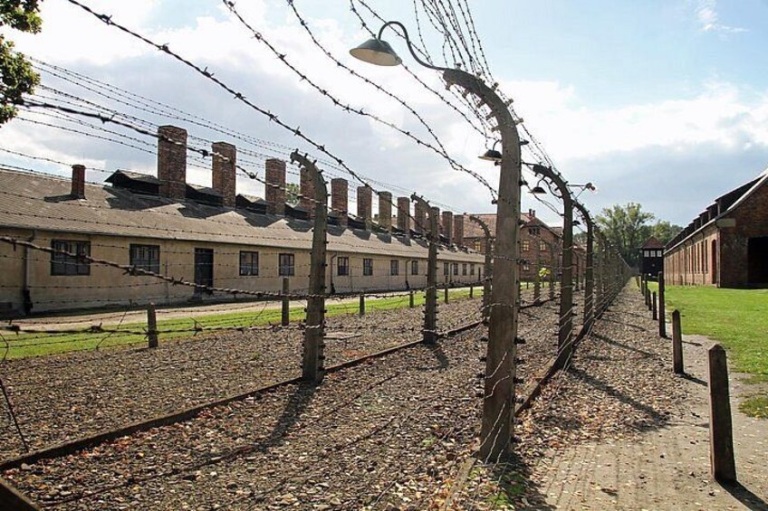 A railway track with barbed wire, a building with chimneys, and a clear sky. 5