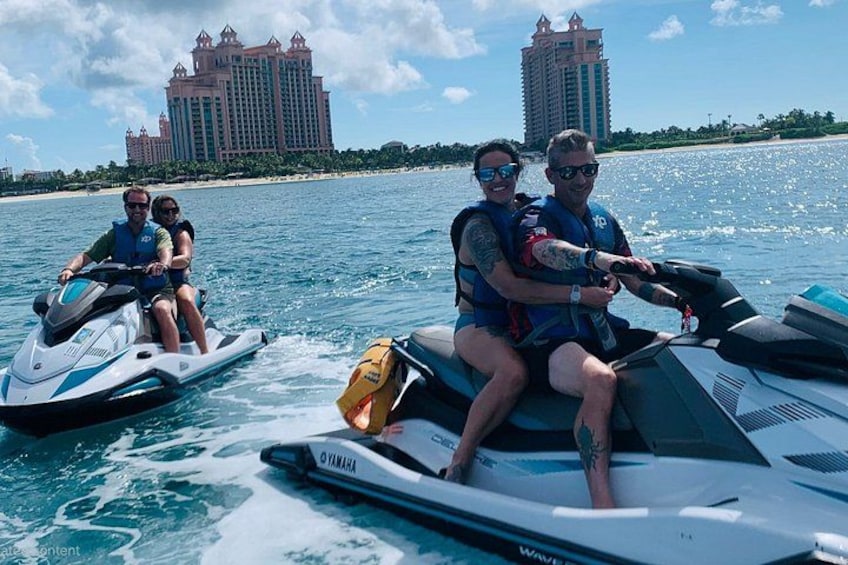 Three people on jet skis on a body of water with a large resort building in the background. 1