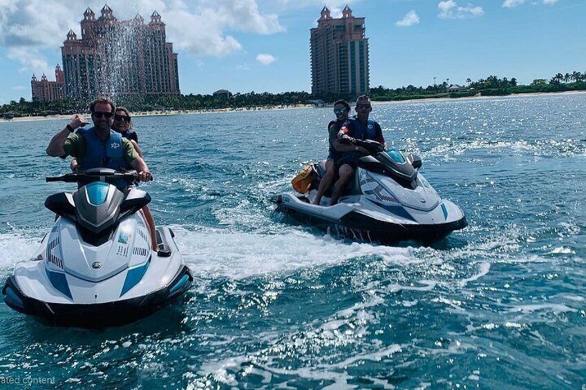 Two jet skis on a body of water with a large hotel in the background. 3