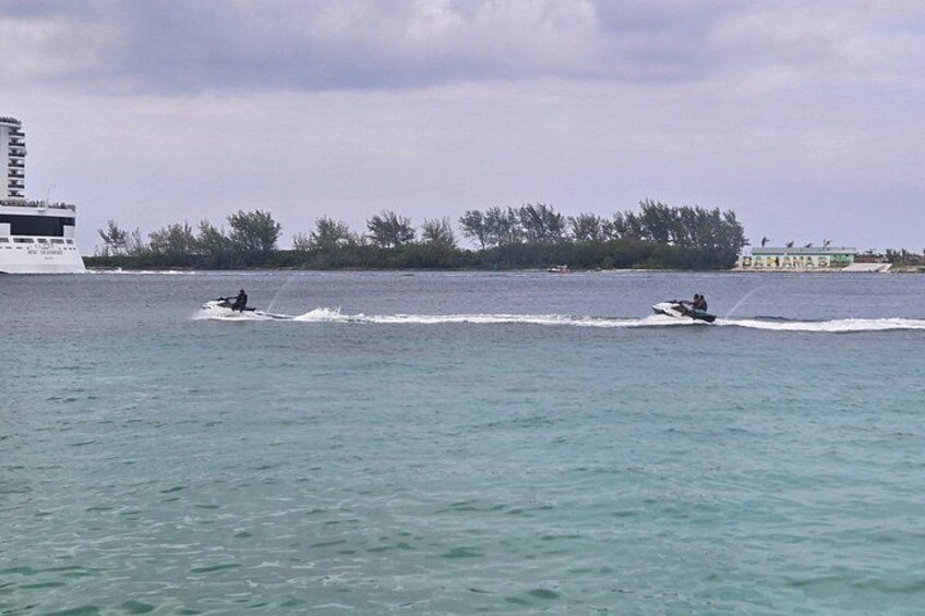 A body of water with two jet skis and a large cruise ship in the background. 2