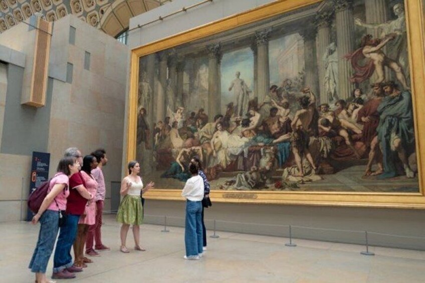 A large classical painting in an indoor gallery with visitors observing it. 1