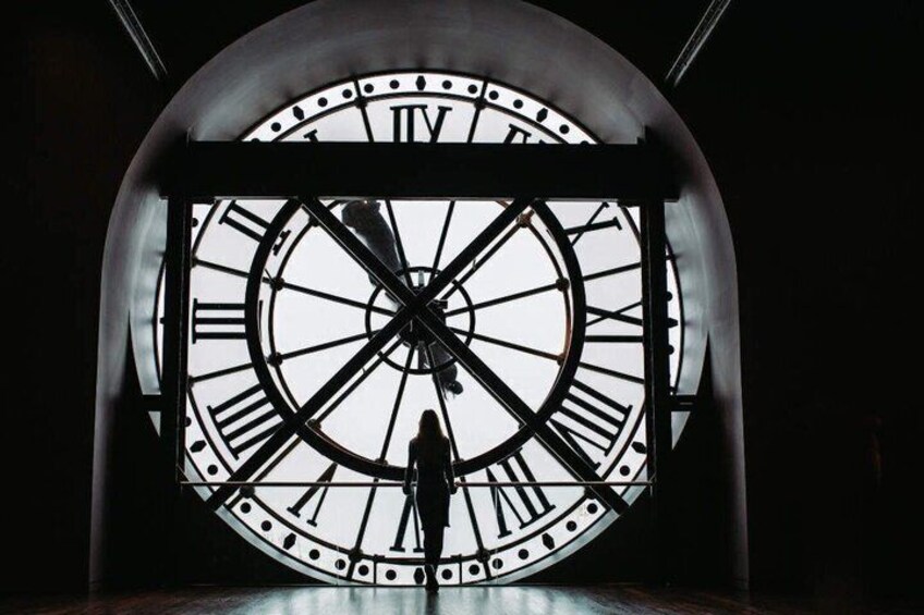 A large clock with Roman numerals and a silhouette of a person in front of it. 5