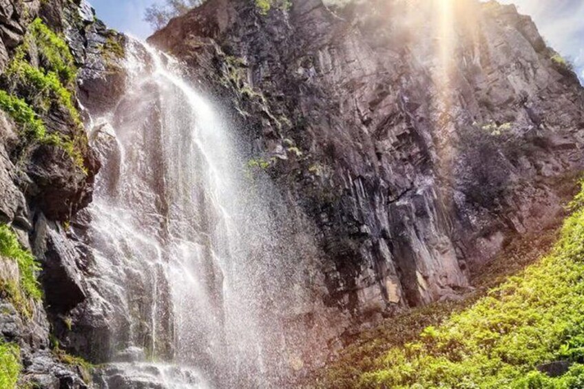 A waterfall cascading down a rocky cliff with lush greenery at the base. 5