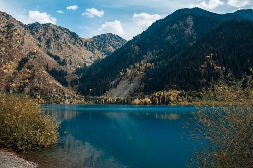 A mountain lake with clear blue water, surrounded by forested hills. 4