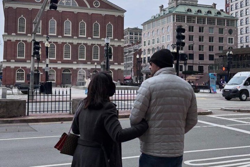 A couple standing at a crosswalk with a historic building in the background. 2