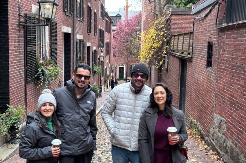 A narrow alley with brick buildings, a person holding a coffee cup, and another person in a white jacket. 5