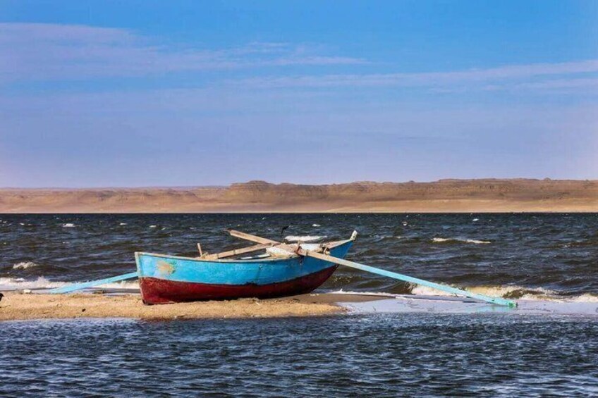 A blue and red boat on a sandy shore with water. 5