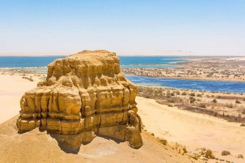 A large rock formation in a desert landscape with a body of water in the background. 2