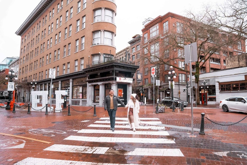 A couple crossing a pedestrian crosswalk in an urban setting with brick buildings and a sign that reads 'BEGIN WAY.' 2