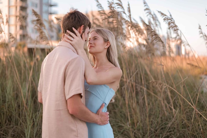A couple embracing in a field with tall grasses and a building in the background. 1