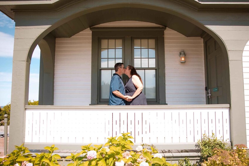 A couple kissing on a porch with a white fence and a window. 4