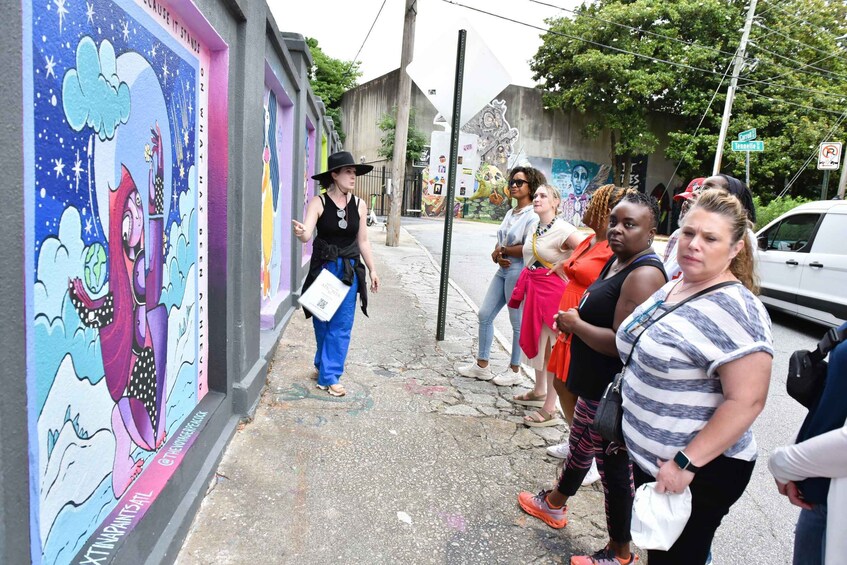 A mural on a wall, a group of people standing on the sidewalk, and a street sign. 5