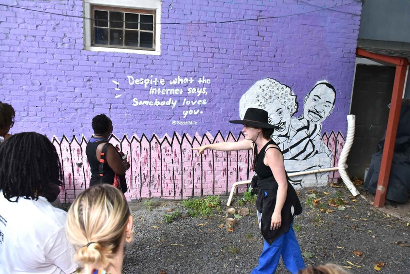 A mural on a purple brick wall with a quote and a drawing of two people. 4