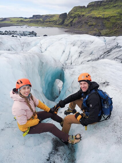 Two people sitting on a glacier with a glacier cave in the background. 2