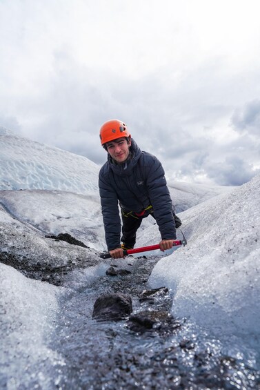 A person in a helmet and jacket breaking ice with a tool. 3