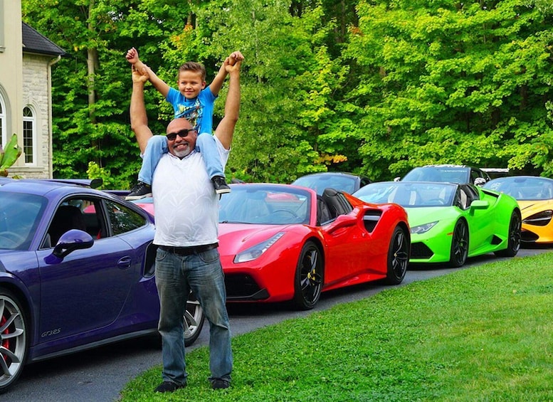 A man carrying a child on his shoulders, with luxury sports cars parked in the background. 2