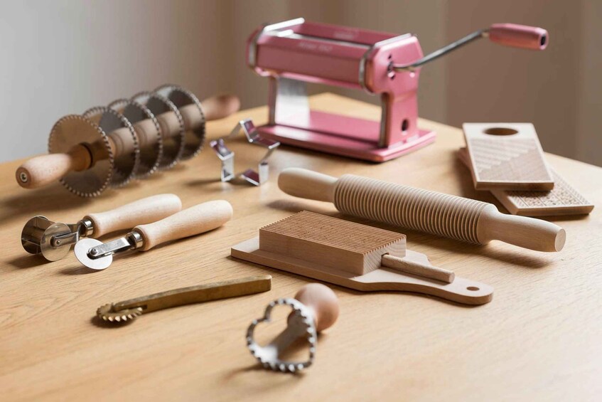 Various kitchen tools, including a pasta maker, rolling pin, and dough cutters on a wooden surface. 2