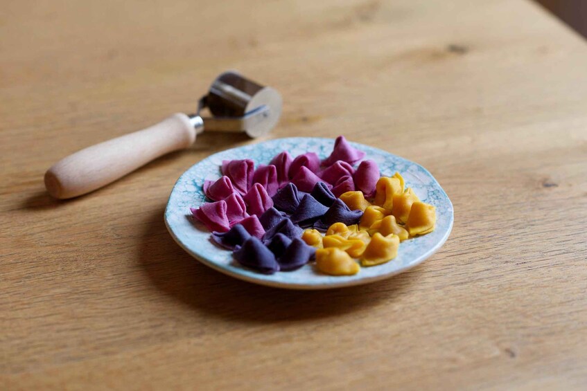 A plate of colorful pasta shapes on a wooden table with a pasta cutter. 3