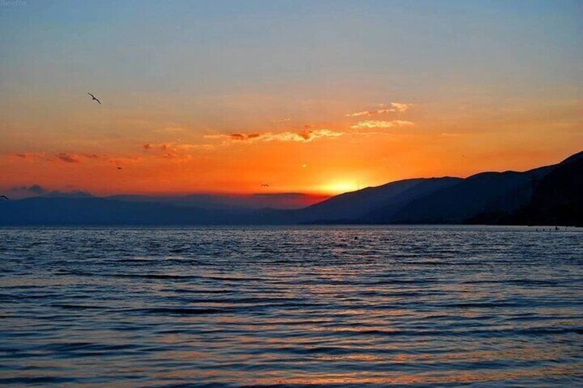 A sunset over a calm sea with silhouettes of mountains in the background. 2