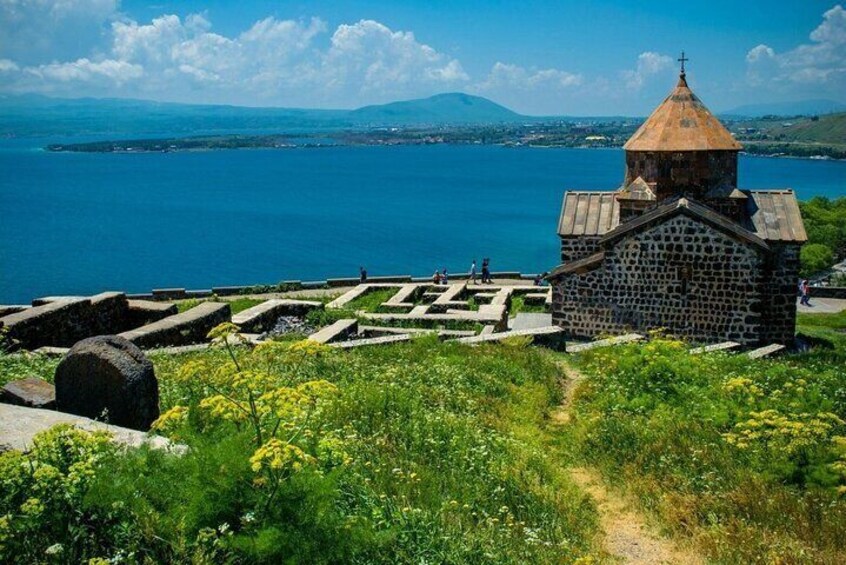 A stone church with a dome, surrounded by a cemetery with headstones, overlooking a body of water and distant mountains. 5