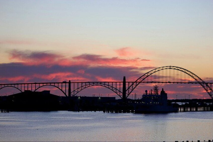 A bridge silhouetted against a sunset sky, with calm water below. 4