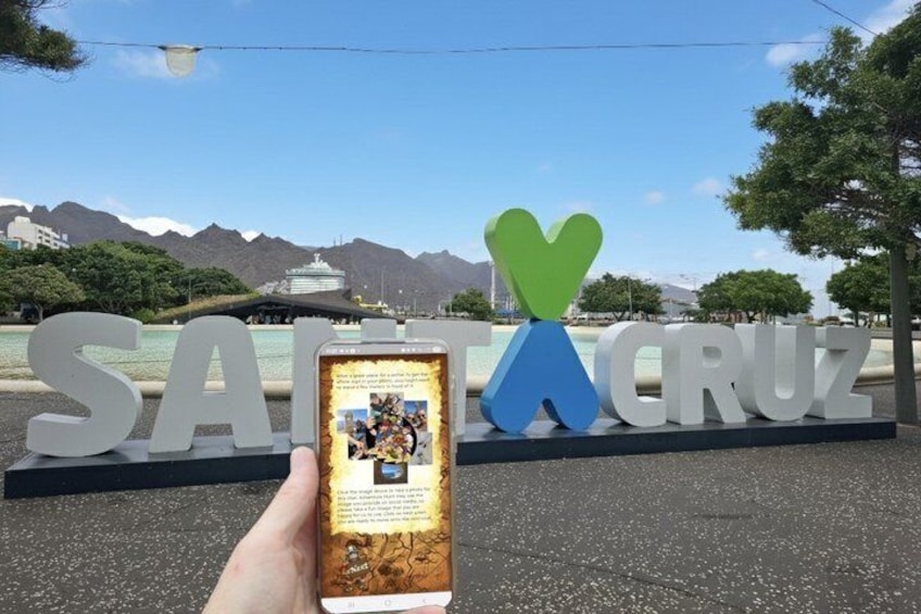 A hand holding a smartphone with a photo of a sign that reads 'SAINT CRUZ' with a heart-shaped design. 1