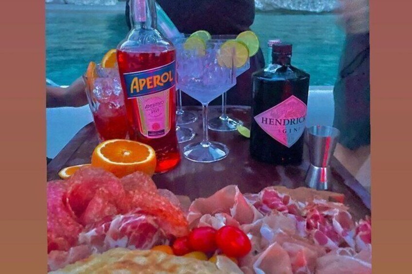 A table with a bottle of Aperol, a bottle of Hendrick's gin, a martini glass, and a variety of meats and fruits. 4
